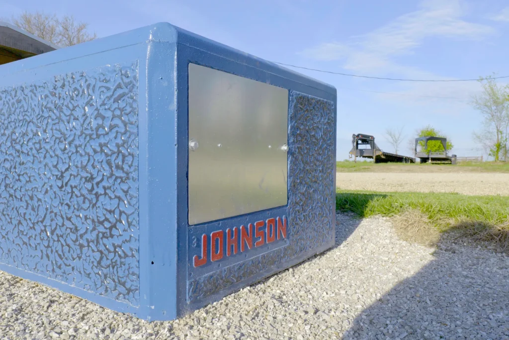 A blue concrete Johnson livestock waterer sitting on a gravel base outdoors at Dutchman’s Farm Supply in Versailles, Missouri.