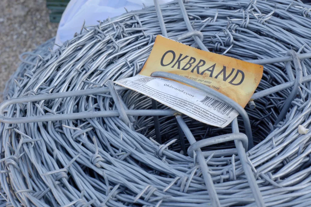 A close-up view of a large roll of galvanized barbed wire with an OK Brand label at Dutchman’s Farm Supply in Versailles, Missouri.